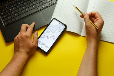 Frame Plus exhibitor calculating booth budget at office desk with laptop and smartphone charts